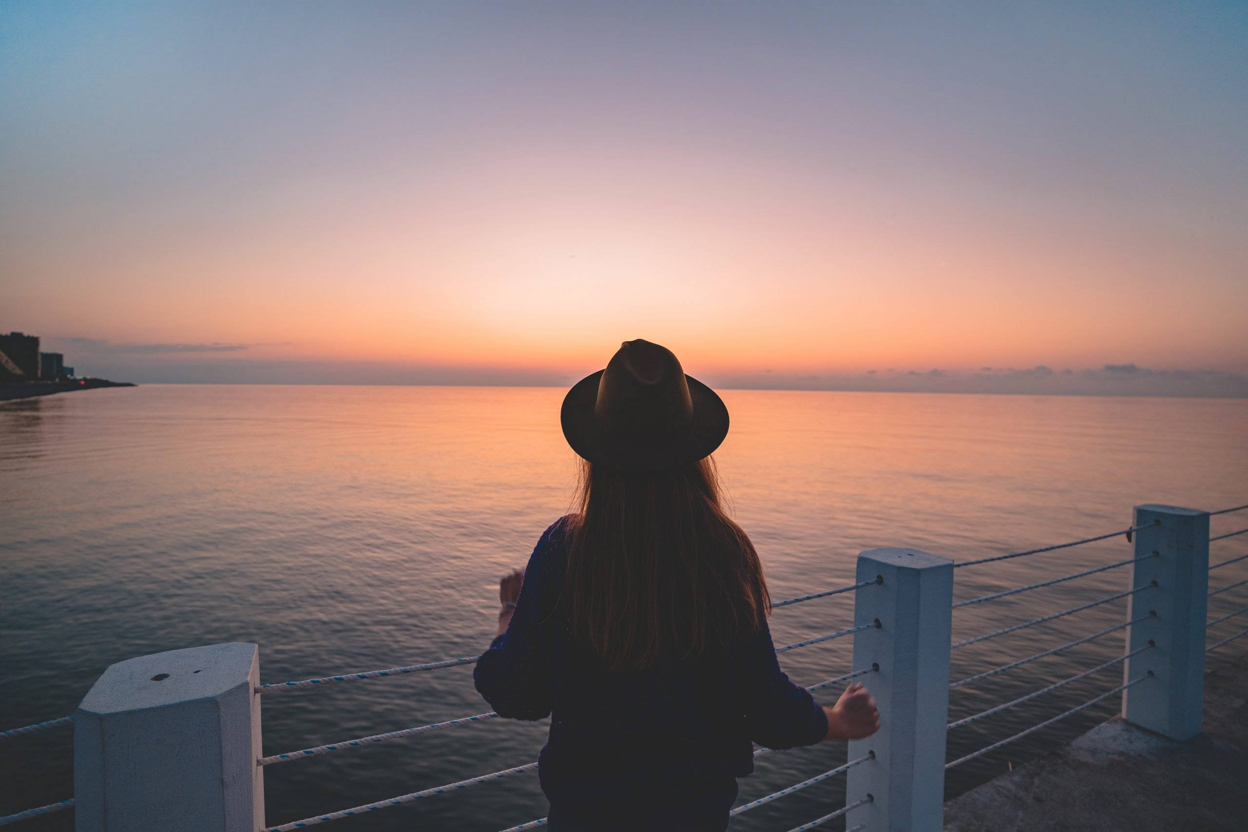One lonely carefree traveler woman in a hat on a sea pier at sun One lonely carefree traveler woman in a hat on a sea pier at sunset. Happy concept, free people and enjoying life