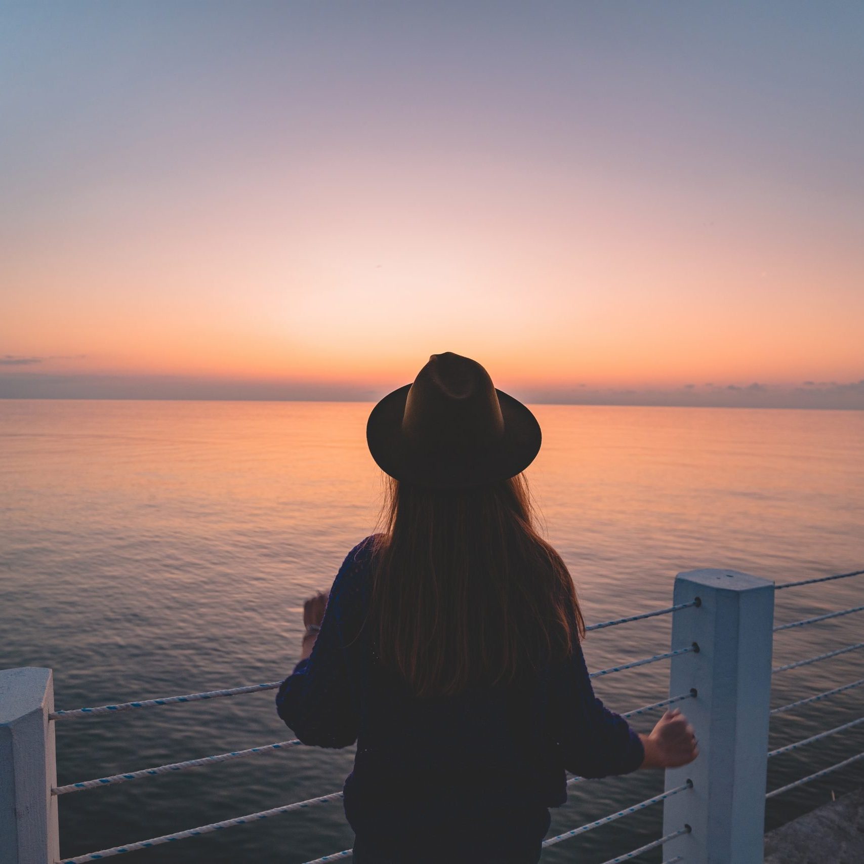 One lonely carefree traveler woman in a hat on a sea pier at sun One lonely carefree traveler woman in a hat on a sea pier at sunset. Happy concept, free people and enjoying life